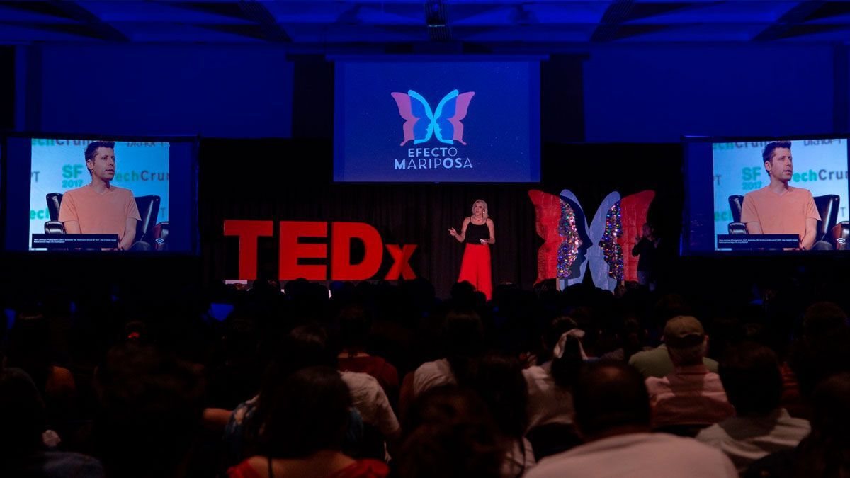 Ophelia en el escenario de TEDx Teopanzolco, con las letras rojas de TEDx y pantallas detrás. Horizontal.